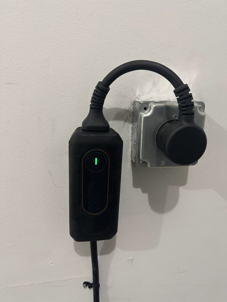 A close-up of an electric vehicle charger plugged into a wall outlet, installed by Black Power Redevelopers in Papillion, NE.