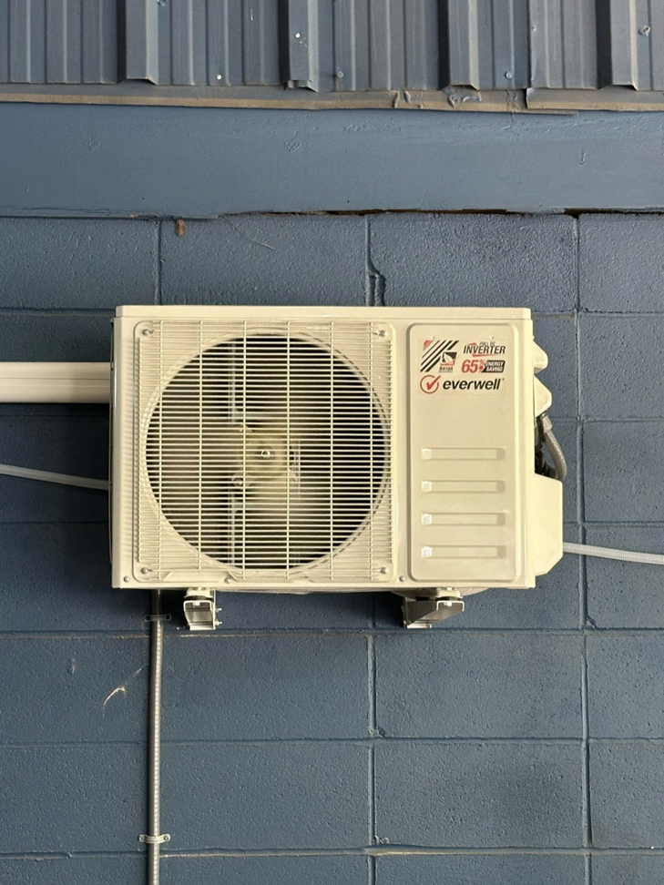 An Everwell outdoor mini-split AC unit installed on a blue block wall by Spartan Air Conditioning in McIntosh, AL.