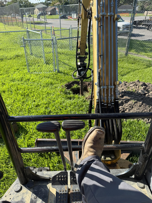 An excavator digging a hole for a utility pole or underground electrical conduit by Relay Electric, LLC in Suffolk, VA.