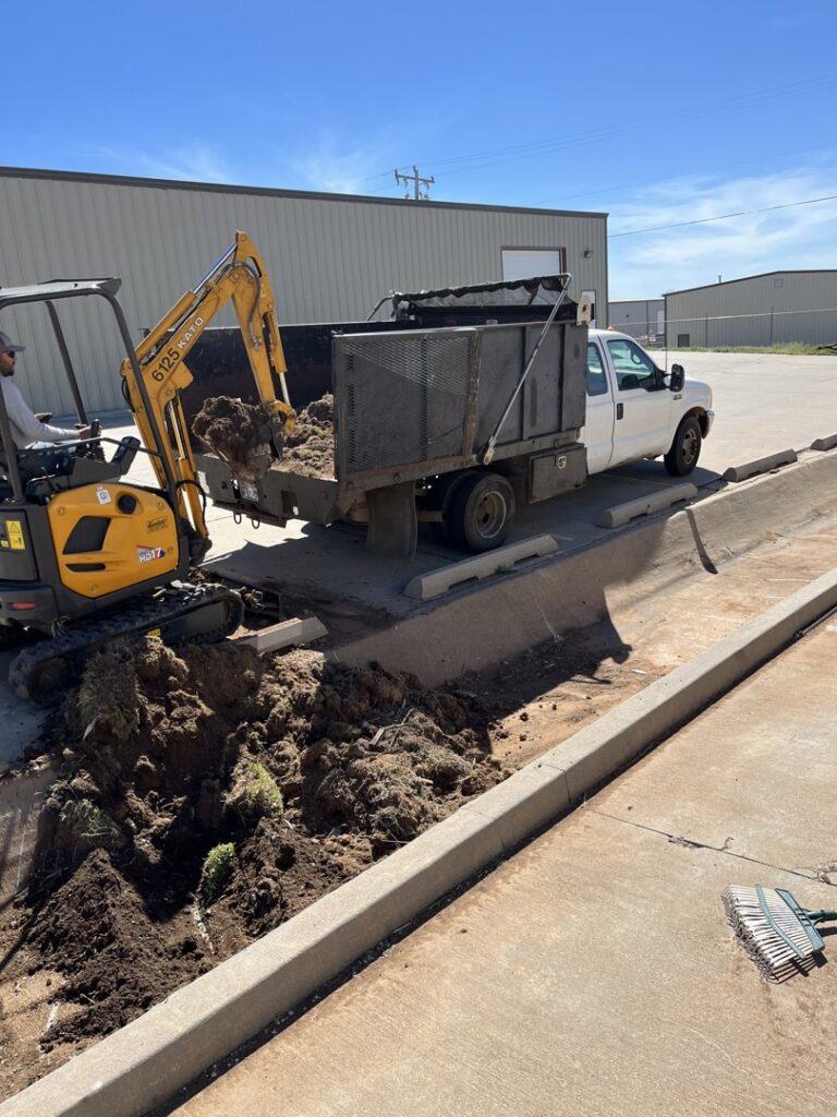 An excavator loading soil and debris into a dump truck during a landscaping project by Perez Lawn Care llc in Oklahoma City, OK