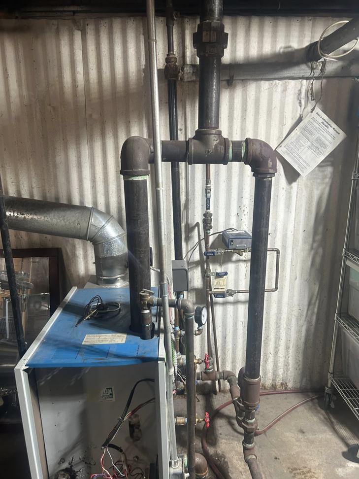 An existing boiler and furnace system with visible piping, serviced by Controlled Weather HVAC in Shelby Township, MI.