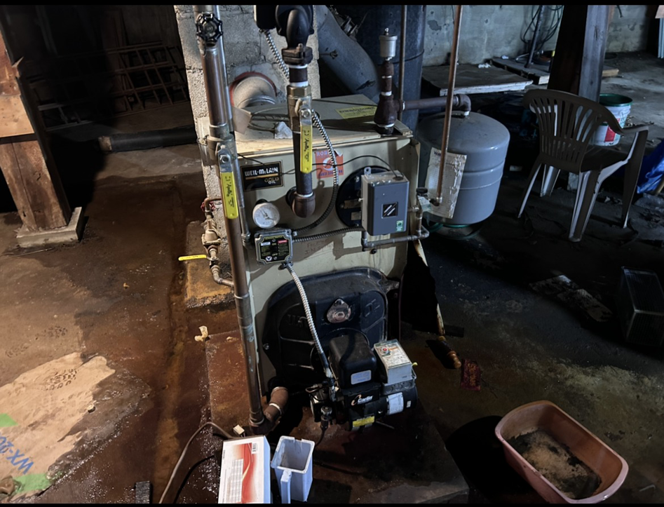 An existing beige boiler heating system with pipes, gauges, and an expansion tank, serviced by HomeStyle Heating and Air LLC in Barrington, NH.