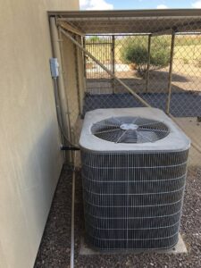 An existing outdoor AC condenser unit next to a building wall, ready for service by Hellerud Air in Peoria, AZ.