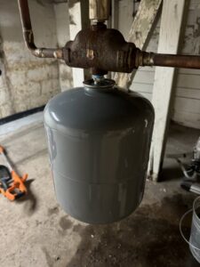 A grey expansion tank connected to copper pipes, part of a heating or water system, installed by Evergreen HVAC Comfort Solutions in Milwaukee, WI.