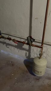 An expansion tank and piping with a pressure gauge, part of a heating system by Tony Marzano Plumbing & Heating LLC in Hartford, CT.