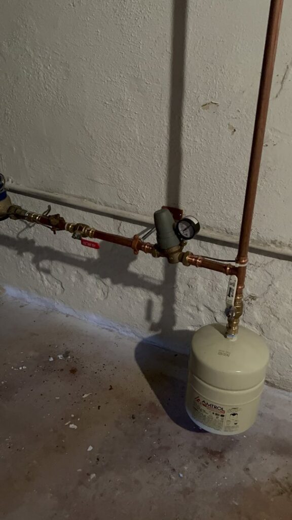 An expansion tank and piping with a pressure gauge, part of a heating system by Tony Marzano Plumbing & Heating LLC in Hartford, CT.