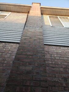 An exterior brick chimney on the side of a house, showing visible cracks that may require inspection or repair by Chimney Usa Inc in Chicago, IL.