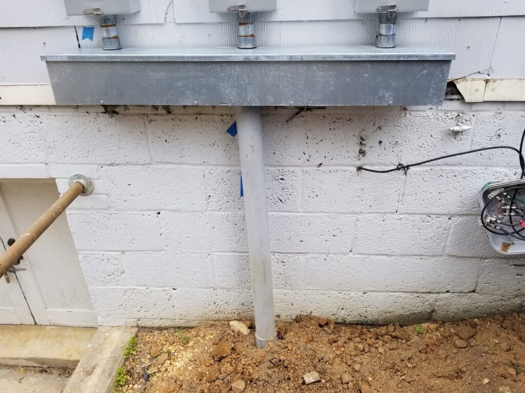 Exterior electrical conduit entering the ground next to a concrete wall, installed by Tim Lambert Electric in Fayetteville, NC.