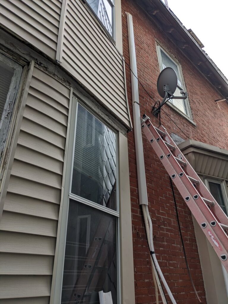 Exterior of a brick house with a ladder and newly installed electrical conduit by GEN3 Electric & HVAC in Philadelphia, PA.