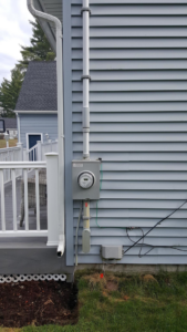 An exterior electrical meter and conduit installed on the side of a house by Benoit Electrical Services in Litchfield, NH.