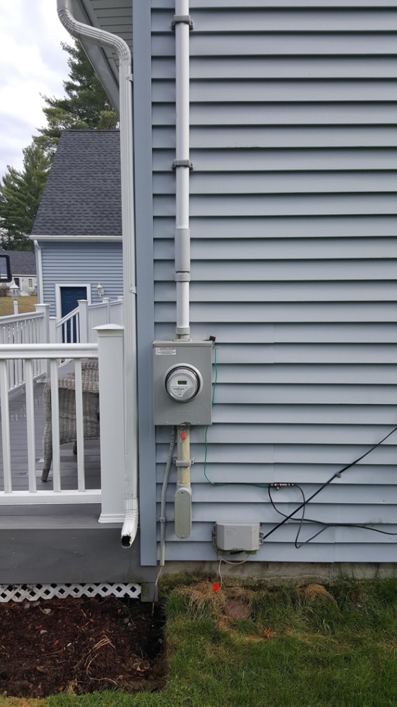 An exterior electrical meter and conduit installed on the side of a house by Benoit Electrical Services in Litchfield, NH.
