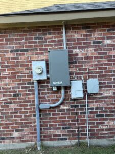 An exterior electrical meter and Kohler transfer switch with conduit installed on a brick wall by Steadfast Electric, LLC in Baton Rouge, LA.