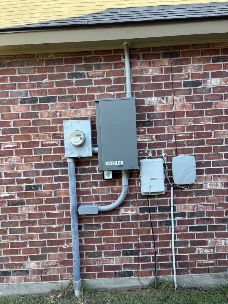 An exterior electrical meter and Kohler transfer switch with conduit installed on a brick wall by Steadfast Electric, LLC in Baton Rouge, LA.
