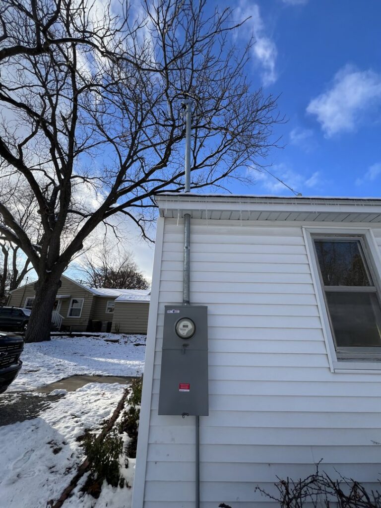 An exterior electrical meter and service mast installation on a house in winter by F&C Electrical Services LLC in Iowa City, IA.