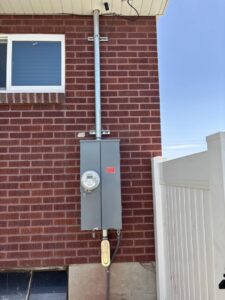 An exterior electrical meter and service panel installation on a brick building by Regal Electrical Services in West Jordan, UT.