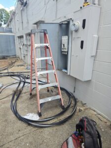 An exterior electrical panel being serviced with cables and a ladder, indicating an upgrade or repair by Apex Electric LLC in Brea, CA.