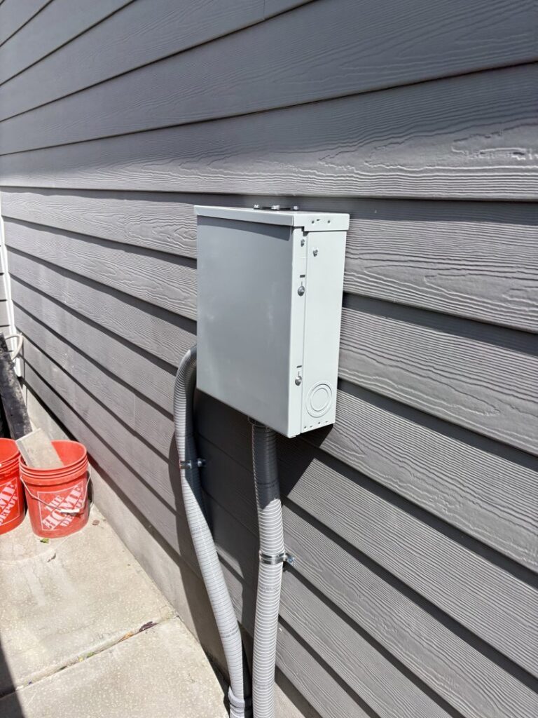 An exterior electrical sub-panel and conduit installation on a building with siding by Regal Electrical Services in West Jordan, UT.