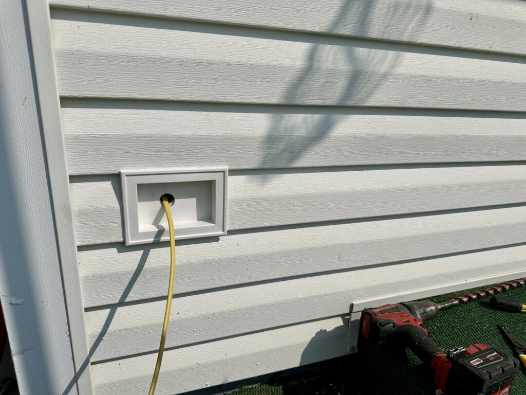 Exterior electrical wiring installation with a yellow cable emerging from a white box, performed by Lighten Up Electric, LLC in Cranston, RI.