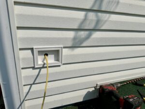 Exterior electrical wiring installation with a yellow cable emerging from a white box, performed by Lighten Up Electric, LLC in Cranston, RI.