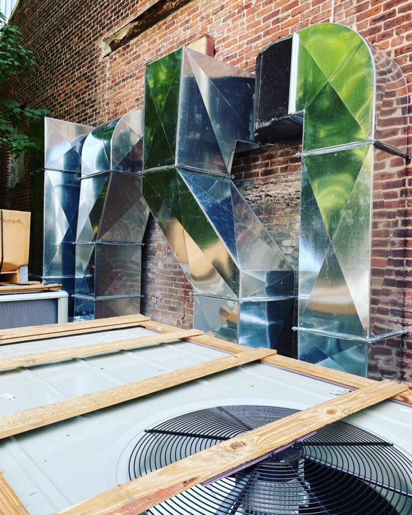 Large exterior metal ductwork and an outdoor AC unit installed on a brick building by Deboque Duct Design Corp. in Staten Island, NY