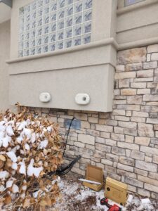 Exterior view of a home showing new HVAC vents and wiring being installed on a snowy day by D & D Heating & Air in Brighton, CO.