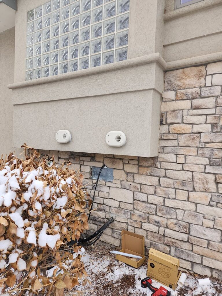 Exterior view of a home showing new HVAC vents and wiring being installed on a snowy day by D & D Heating & Air in Brighton, CO.