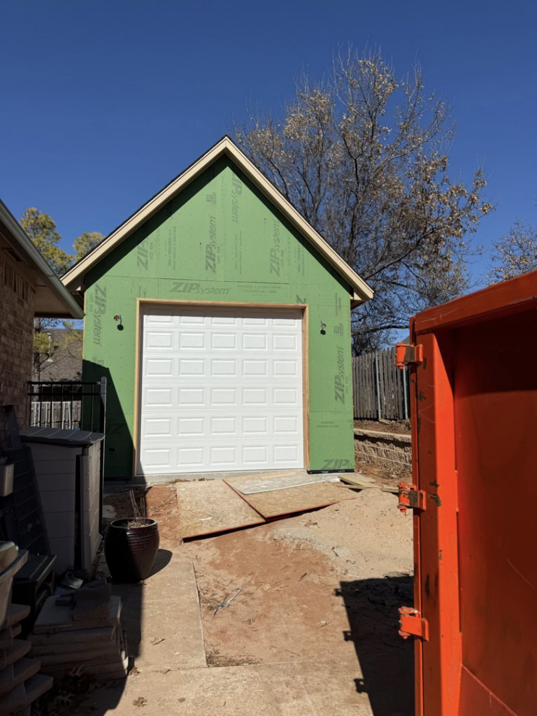 A new white garage door installed on the exterior of a residential garage under construction by Rhino Garage Doors LLC OKC in Edmond, OK.