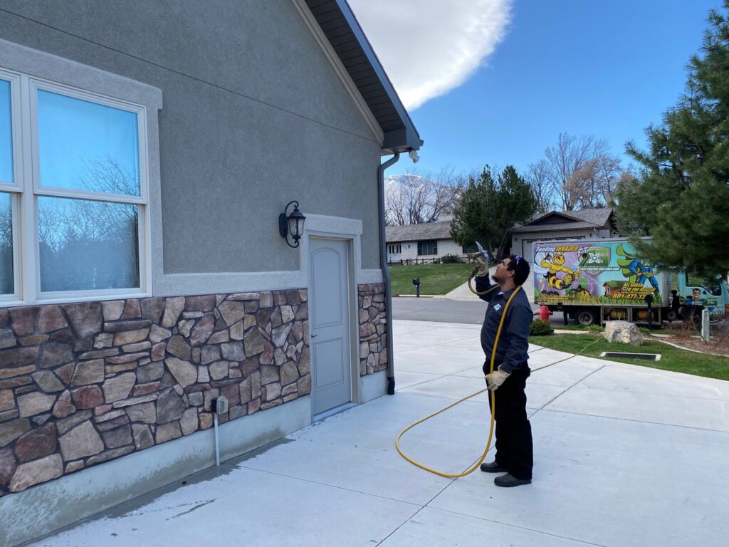 A pest control technician applying exterior treatment to a house by All Green Pest Control and Lawn Care in Provo, UT.