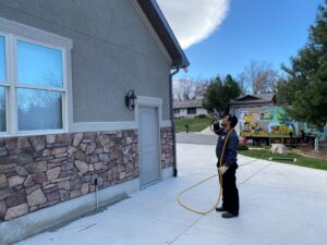 A pest control technician applying exterior treatment to a house by All Green Pest Control and Lawn Care in Provo, UT.