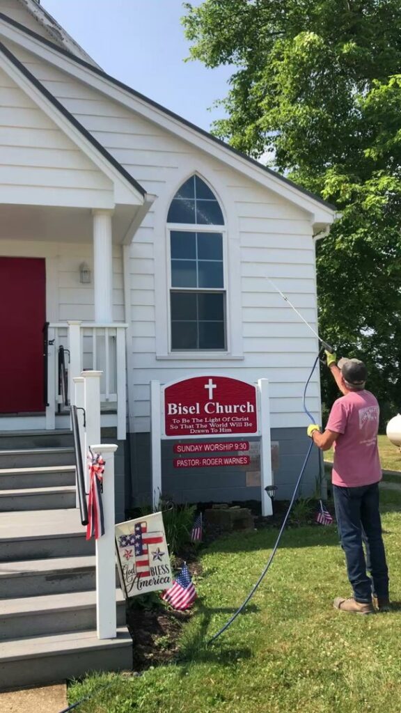 A technician performing exterior pest treatment on a church building with a sprayer for Antix Pest Control in Canton, OH.