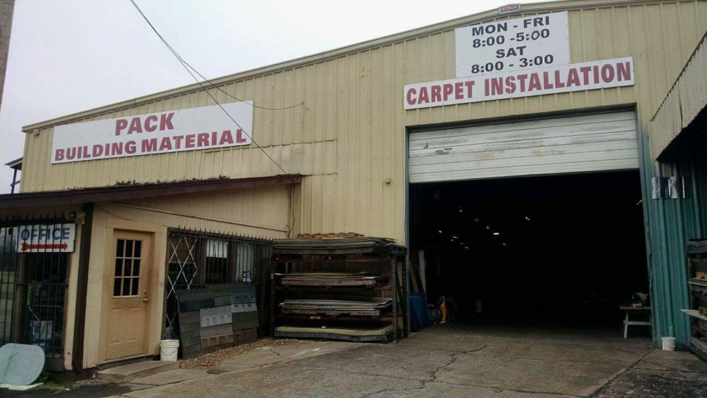 Exterior view of Pack's Building Materials in Fort Smith, AR, with a sign advertising carpet installation services.