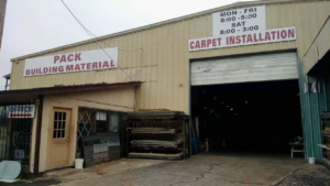 Exterior view of Pack's Building Materials in Fort Smith, AR, with a sign advertising carpet installation services.