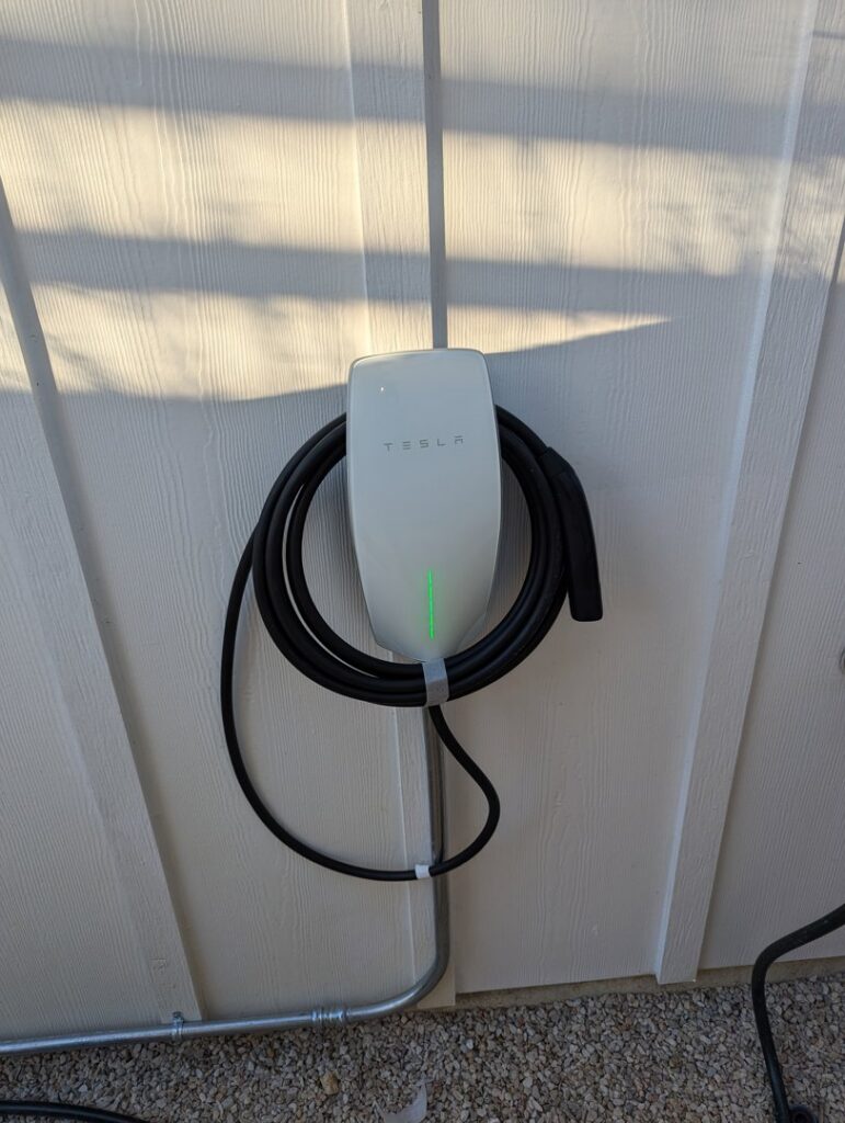 An exterior Tesla EV charger installation on a house wall with conduit, provided by Davis Electric in Cleveland, OH.