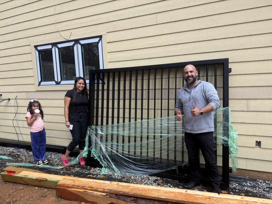 A family standing next to their new black metal gate delivered by All With Us LLC in Green Cove Springs, FL.