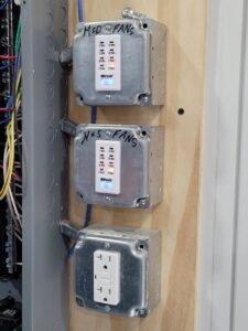 Fan timers and a GFCI outlet installed on a wooden panel by FOXX & Hounds Electric in Sioux City, IA.