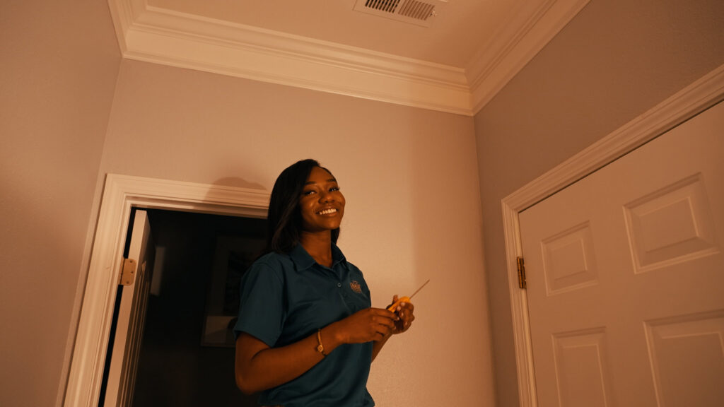A female HVAC technician smiling while working on a ceiling vent at a client's home for Relief Heating and Cooling, LLC in Greensboro, NC.