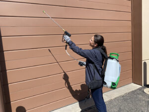 A female technician spraying the exterior of a commercial building with a backpack sprayer for Pest Free Rochester in Rochester, MN.