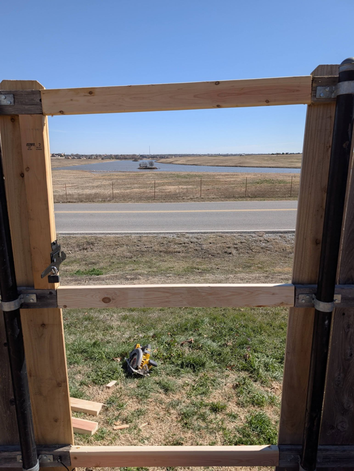 A wooden fence gate frame under construction by Black and Sons fencing in Indiahoma, OK, with a view of the landscape.