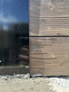 A close-up of a black metal fence post base where it meets concrete, with horizontal wood planks installed by MJ Custom Fencing in Las Cruces, NM.