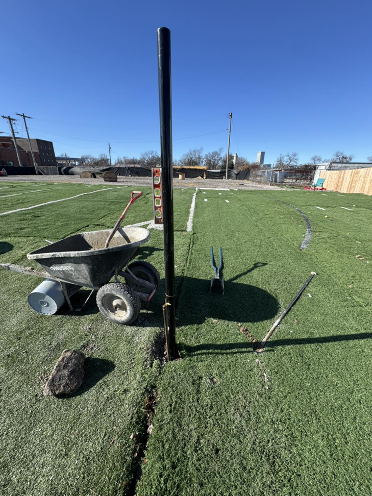 A fence post being installed with a level and tools on an artificial turf field by Just Handy Fence and Stain LLC in Tulsa, OK.