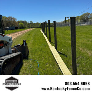 Fence posts and horizontal boards laid out for installation with a skid steer nearby by Kentucky Fence Co in McConnells, SC.