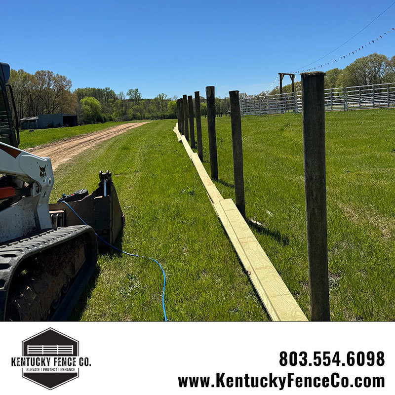 Fence posts and horizontal boards laid out for installation with a skid steer nearby by Kentucky Fence Co in McConnells, SC.