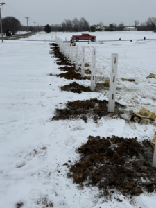 White fence posts being installed in a snowy landscape, showing a fencing project by Henderson Fence in Culpeper, VA.
