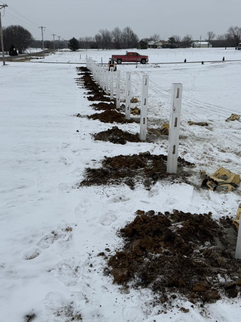 White fence posts being installed in a snowy landscape, showing a fencing project by Henderson Fence in Culpeper, VA.