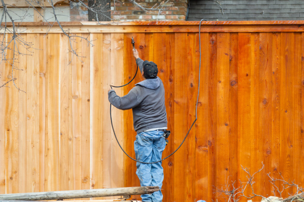A professional applying stain to a wooden fence with a sprayer, showcasing work by Walt's Fence Staining in Allen, TX.