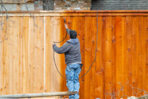 A professional applying stain to a wooden fence with a sprayer, showcasing work by Walt's Fence Staining in Allen, TX.