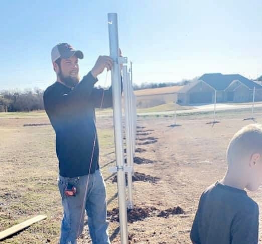 A fencing contractor installing new metal fence posts for a property in Stillwater, OK, by Pokey Fencing & Masonry.