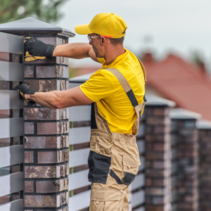 A fencing contractor from Newcastle Fencing in Renton, WA, installing a modern brick and metal fence.