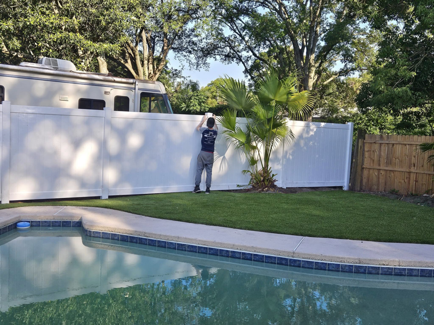A fencing contractor from Geo's Custom Fencing, LLC installing a white vinyl fence near a pool in Jacksonville, FL.