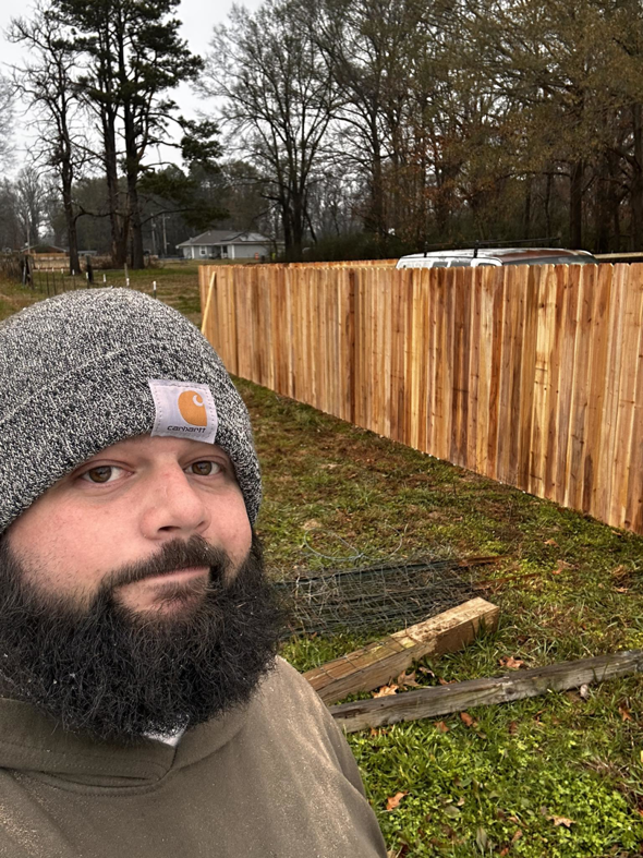 A fencing contractor standing in front of a newly installed wood fence by Holland Fences and Decks in Bartlett, TN.